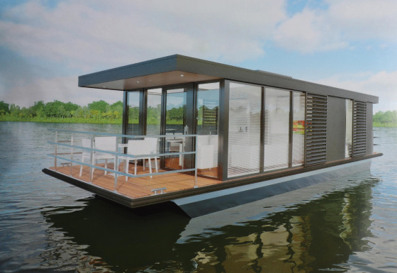 Moderne Houseboat Refugio ses på vandet, omgivet af grøn natur og blå himmel, med en åben terrasse.