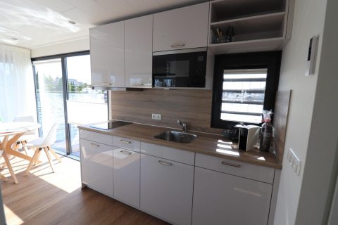 Cucina moderna sulla houseboat «Refugio» nei Paesi Bassi con ampie finestre e area pranzo luminosa.