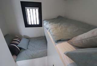 Dos pequeñas camas con sábanas verdes en la Houseboat «Refugio» en Países Bajos, junto a la ventana.