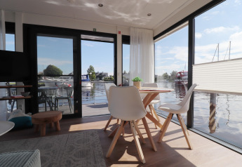 Vista interna dell'houseboat 'Refugio' nei Paesi Bassi con zona pranzo moderna vicino all’acqua.