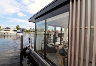 Vue de la péniche «Refugio» aux Pays-Bas avec ses murs en verre, son intérieur moderne et des bateaux autour.