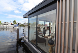 Udsigt til Houseboat «Refugio» i Holland med glasvægge, moderne indretning og både på vandet.