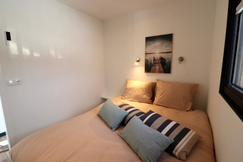 Chambre moderne sur la péniche Refugio aux Pays-Bas avec lit beige, coussins décoratifs et tableau mural.