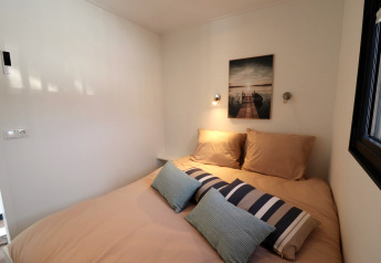 Chambre moderne sur la péniche Refugio aux Pays-Bas avec lit beige, coussins décoratifs et tableau mural.