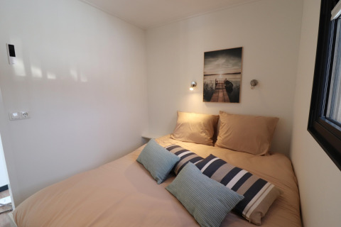 Dormitorio moderno en la casa flotante Refugio en los Países Bajos con cama beige, cojines y cuadro decorativo.