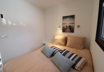 Chambre moderne sur la péniche Refugio aux Pays-Bas avec lit beige, coussins décoratifs et tableau mural.