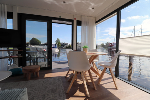 Intérieur moderne et lumineux du houseboat Refugio avec grandes fenêtres sur l’eau aux Pays-Bas.