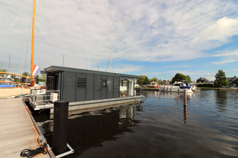 Das moderne Hausboot Refugio liegt an einem Steg in den Niederlanden, umgeben von Wasser und Booten.