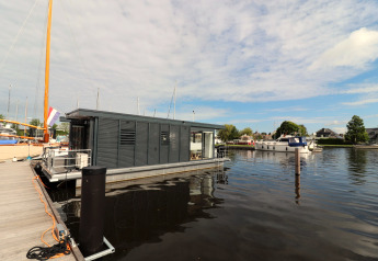 Modern houseboat Refugio docked at a marina in the Netherlands, surrounded by water and sailing boats.