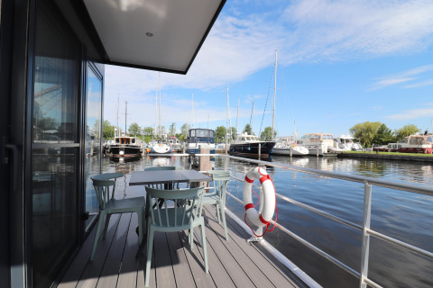 Udsigt fra Houseboat Refugio med terrasse, borde og stole, der vender ud mod både og marina i Holland