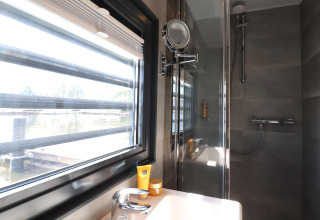 Baño con ducha, ventana grande y vista al agua en la casa flotante Refugio en los Países Bajos.