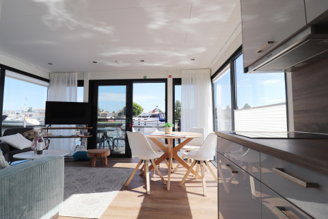 Interno luminoso e moderno della houseboat 'Refugio' nei Paesi Bassi con grandi finestre e vista sul porto.