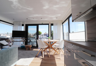 Interno luminoso e moderno della houseboat 'Refugio' nei Paesi Bassi con grandi finestre e vista sul porto.