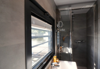 Modern bathroom aboard Houseboat 'Refugio' in the Netherlands with large window, sink, and shower.