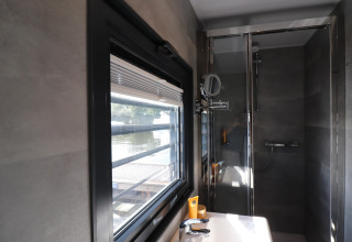 Moderne badkamer op woonboot 'Refugio' in Nederland met groot raam, lavabo en douche.