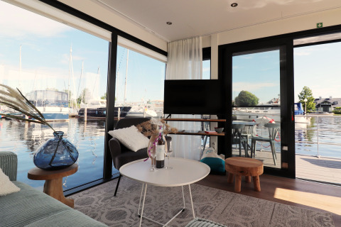 Salon du houseboat 'Refugio' aux Pays-Bas, vue sur marina à travers grandes baies vitrées.