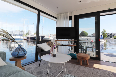 Wohnbereich auf dem Hausboot 'Refugio' in den Niederlanden mit Blick auf Yachthafen und Wasser.