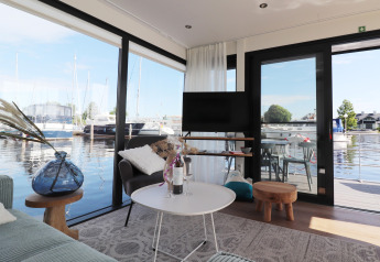 Salon du houseboat 'Refugio' aux Pays-Bas, vue sur marina à travers grandes baies vitrées.