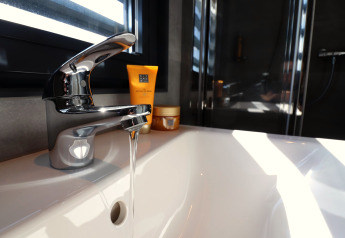 Moderner Wasserhahn mit fließendem Wasser auf dem Hausboot Refugio in den Niederlanden, Sonnenlicht durchs Fenster.