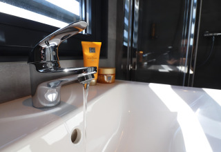 Moderne vask med rindende vand og spejlrefleksion på Houseboat Refugio i Nederlandene, sollys skinner ind.