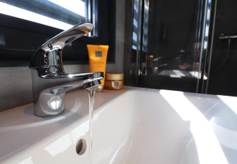 Robinet moderne avec eau courante sur Houseboat Refugio aux Pays-Bas, lumière du soleil entrant par la fenêtre.