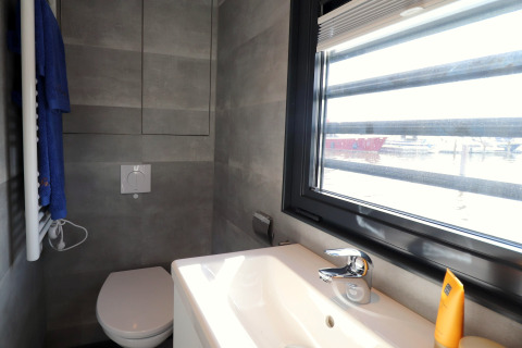 Modernes Badezimmer im Hausboot Refugio in den Niederlanden mit WC, Waschbecken und Blick aufs Wasser.