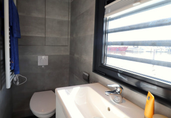 Modern bathroom on Houseboat Refugio in the Netherlands, showing toilet, sink, and large window facing marina.