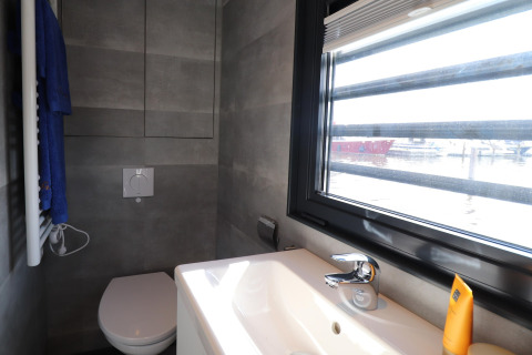 Moderne badeværelse på Houseboat Refugio i Holland med toilet, håndvask og stor vindue mod havnen.