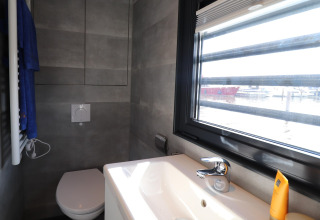 Baño moderno en la Houseboat Refugio en los Países Bajos, con inodoro, lavabo y ventana grande al puerto.