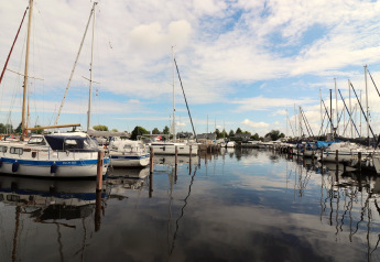Blick von Hausboot 'Refugio' in den Niederlanden auf Segelboote im Hafen unter blauem Himmel.