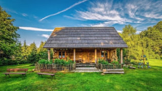 Uno chalet in legno immerso nel verde, circondato da fiori e panchine, sotto un cielo limpido e sereno.