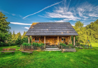 Un chalet en bois charmant entouré de pelouse verte, de fleurs et de bancs, sous un ciel bleu éclatant.