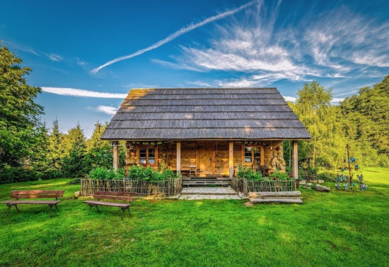 Een gezellig houten huisje op het platteland, met bloemen, bankjes en gras onder een stralende lucht.