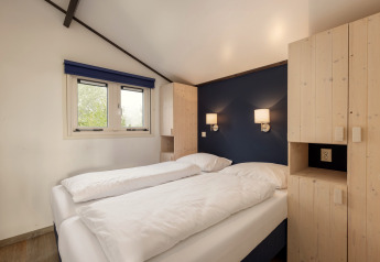 Camera luminosa con letto matrimoniale, parete blu e armadi in legno nello chalet Water park Terkaple 2, Paesi Bassi.