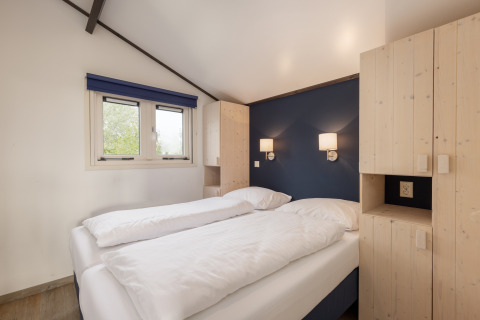 Helles Schlafzimmer mit Doppelbett, blauer Wand und Holzschränken im Chalet Water park Terkaple 2, Niederlande.