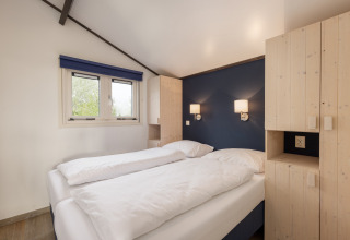 Lyst soveværelse med dobbeltseng, blå væg og moderne belysning i chalet Water park Terkaple 2 i Nederlandene.