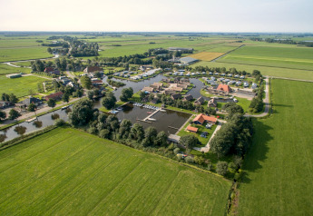 Vista aerea di un villaggio di chalet con porto, campi verdi circostanti e paesaggio rurale tranquillo.