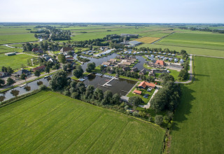 Luftfoto af et charmerende feriechaletanlæg med bådehavn, grønne marker og fredelige landskaber.