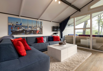 Woonruimte in chalet Water park Terkaple 2 Nederland met comfortabele zetel, rode kussens en terras.