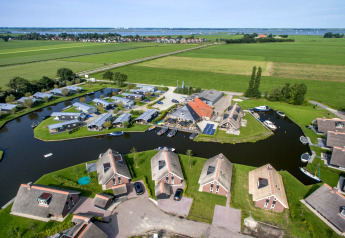 Aerial view of modern chalets by a canal, surrounded by green fields and water, picturesque rural setting.