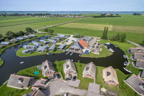 Vista aerea di chalet moderni su un canale, circondati da campi verdi e acqua, ambiente rurale pittoresco.
