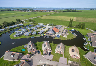 Vista aérea de chalets modernos junto a un canal, rodeados de campos verdes y agua, entorno rural idílico.