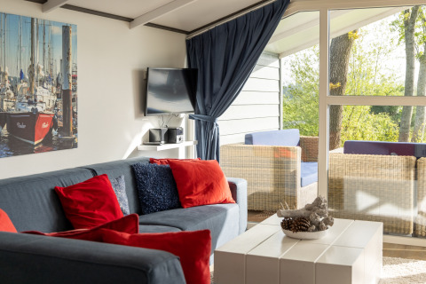Stue i chalet på Water park Terkaple 2 i Holland med blå sofa, røde puder og udsigt til terrasse.