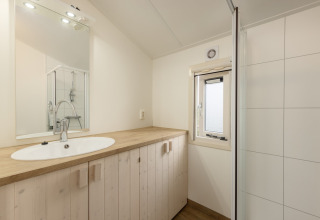 Helles Badezimmer mit Holzwaschtisch, Spiegel und Dusche im Chalet Water park Terkaple 2, Niederlande.