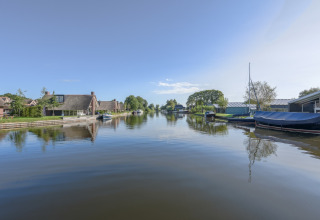 Udsigt over en rolig kanal med både og charmerende chalet-huse på begge sider under en klar himmel.