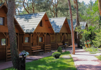 Fila de acogedoras cabañas Holiday cottages Łazy de madera en el bosque con flores y sendero soleado.