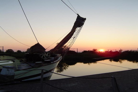 Billede af en båd ved en chalet, fortøjet ved en rolig sø, med solnedgang og reflektioner i vandet.