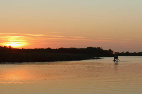 Beautiful sunset view from a chalet, with a person paddleboarding on the calm lake among peaceful scenery.
