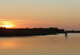 Tramonto mozzafiato visto da un chalet, con una persona che rema sul lago calmo in un ambiente sereno.