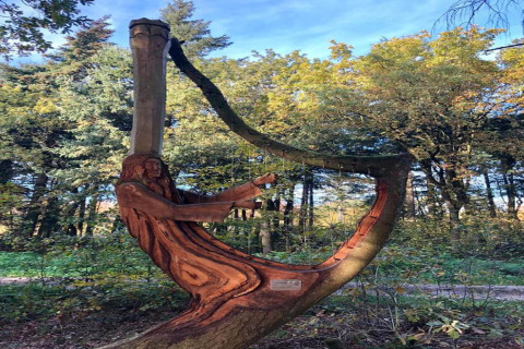 Udskåret træskulptur af en mand, der spiller harpe, integreret i et træ i en skov nær et chalet.